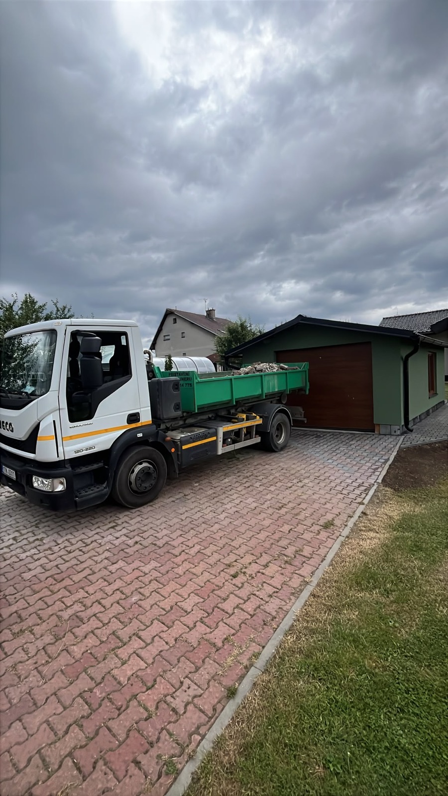 Nosič IVECO přistavuje zelený kontejner na příjezdovou cestu u rodinného domu